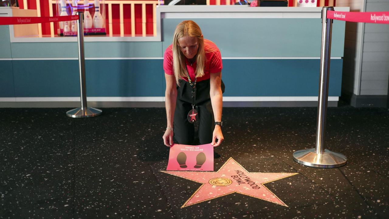 Eine blonde Frau beugt sich über einen rosa Stern und hält ein Plakat mit zwei Fußabdrücken hoch. Eine blonde Frau beugt sich über einen rosa Stern und hält ein Plakat mit zwei Fußabdrücken hoch.