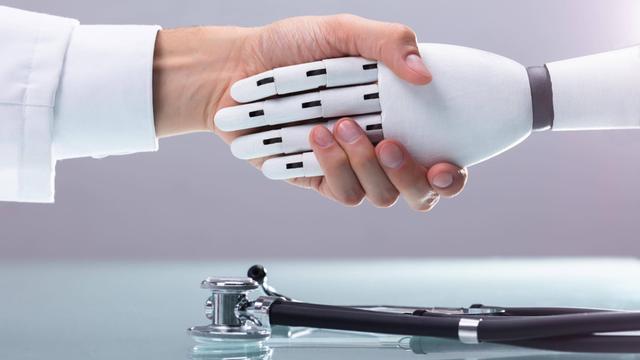 Handschlag einer menschlichen und einer Roboterhand, auf dem Tisch darunter liegt ein Stethoskop