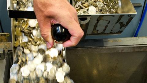 Ein Mann lässt in der staatlichen Münze Baden-Württemberg frisch geprägte Zwei-Euro-Stücke in eine Wanne ab.