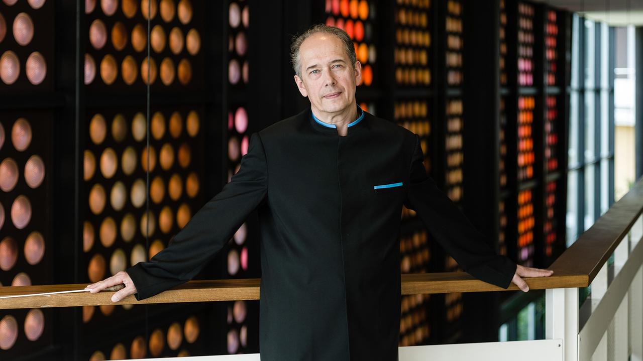 Der Dirignet steht im Foyer der Berliner Philharmonie vor bunten Glasaugen-Fenstern. Der Dirignet steht im Foyer der Berliner Philharmonie vor bunten Glasaugen-Fenstern.