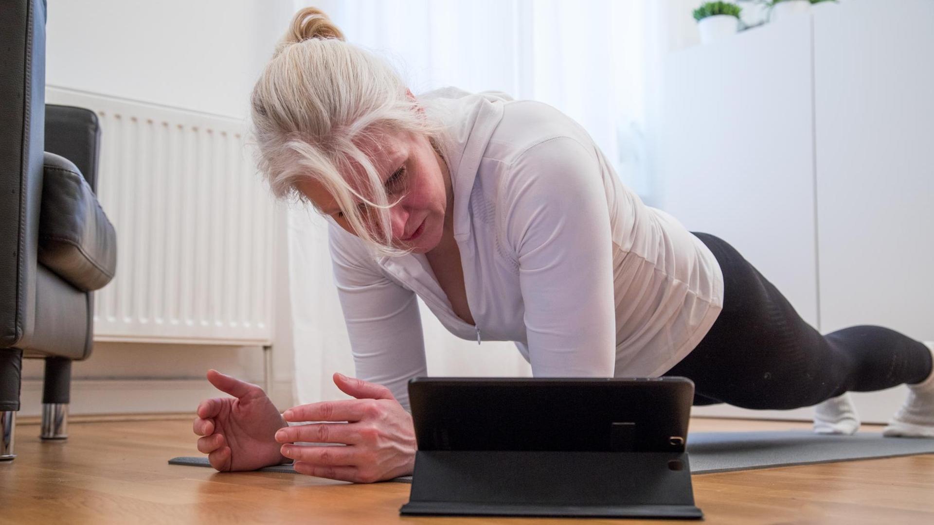 Eine Frau guckt ein Sport-Video und macht die Übungen im Wohn-Zimmer nach. Eine Frau guckt ein Sport-Video und macht die Übungen im Wohn-Zimmer nach.