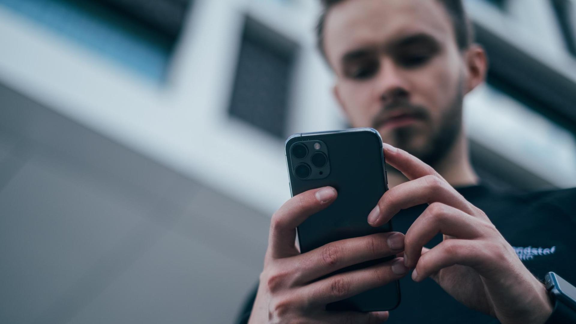 Von unten fotografierter junger Mann, der in seinen Händen ein Smartphone hält und auf dessen Bildschirm blickt. Von unten fotografierter junger Mann, der in seinen Händen ein Smartphone hält und auf dessen Bildschirm blickt.