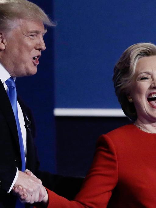 Donald Trump und Hillary Clinton stehen gemeinsam auf der Bühne und schütteln sich dieHand.