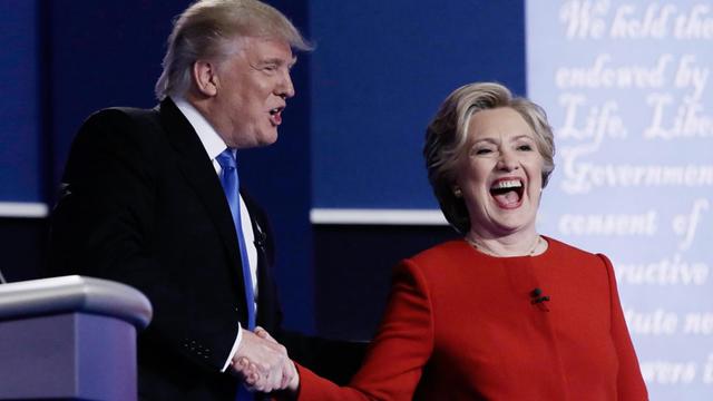 Donald Trump und Hillary Clinton stehen gemeinsam auf der Bühne und schütteln sich dieHand.