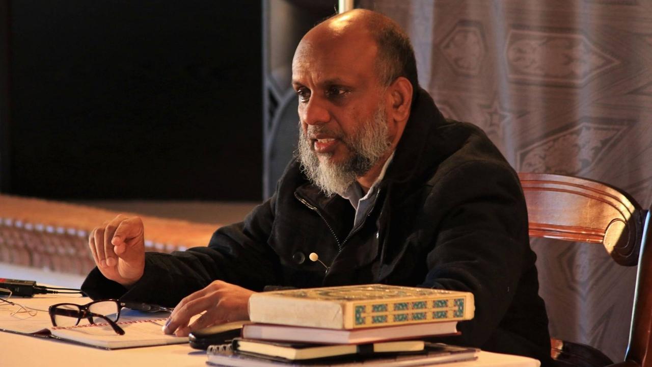 Mohammad Akram Nadwi sitzt im Gespräch an einem Tisch mit unteschiedlichen Schriften und Büchern.