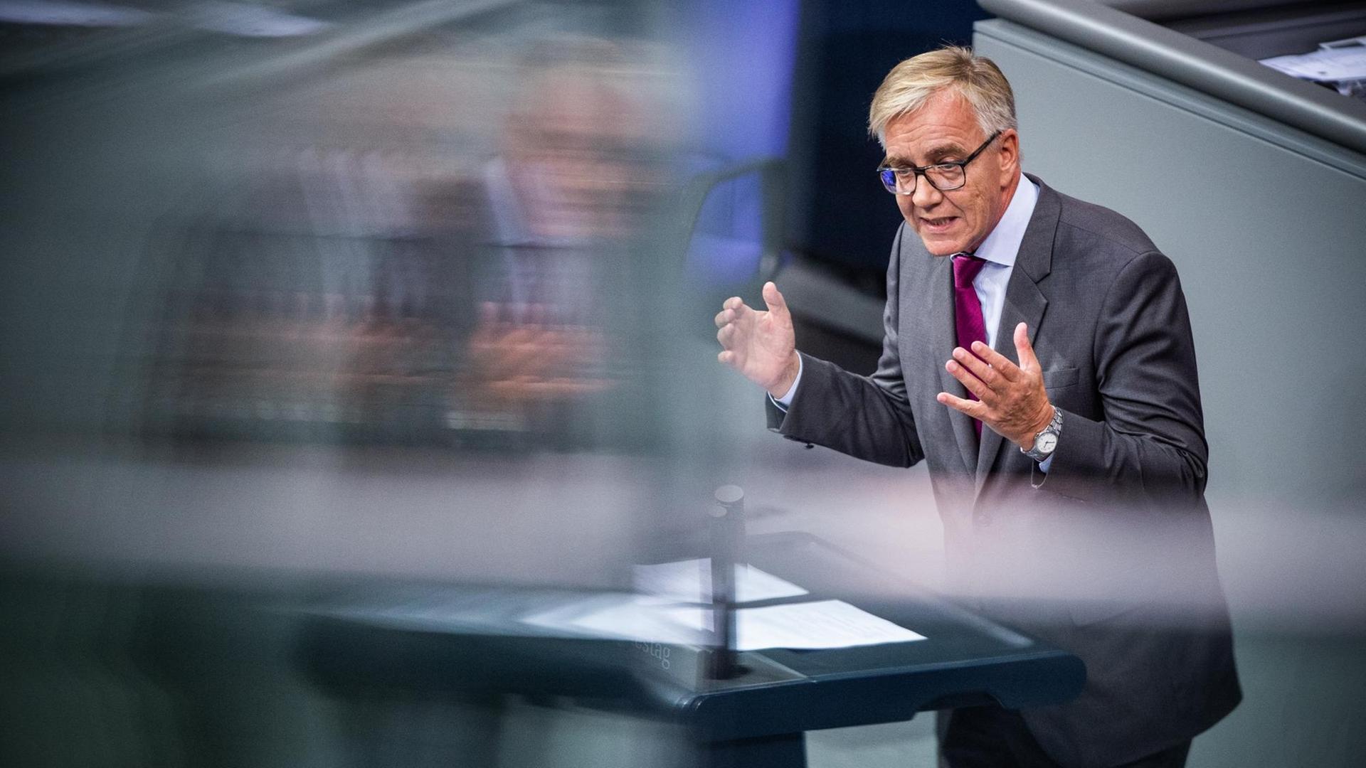 Bartsch spricht und gestikuliert am Rednerpult, er spiegelt sich dabei undeutlich in einer Scheibe. Bartsch spricht und gestikuliert am Rednerpult, er spiegelt sich dabei undeutlich in einer Scheibe.