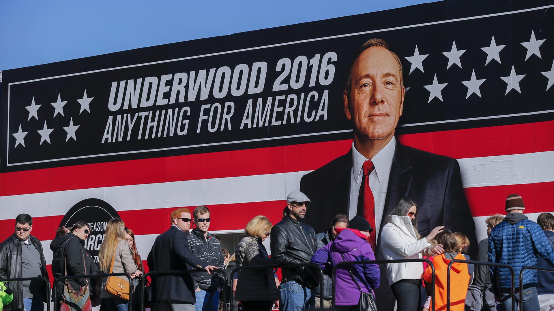 Menschen stehen in einer Schlange vor einem Werbeschild von "House of Cards". Menschen stehen in einer Schlange vor einem Werbeschild von "House of Cards".