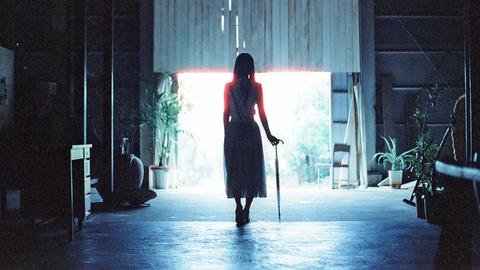 Eine junge Frau mit einem Regenschrim geht auf einen hellen Ausgang zu.