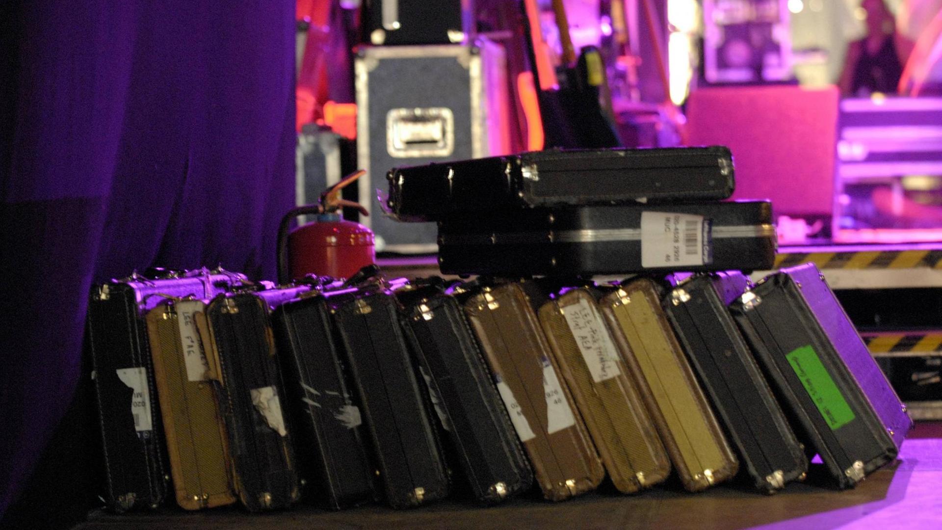 Gitarrenkoffer liegen nebeneinander vor einer hell erleuchteten Bühne. Gitarrenkoffer liegen nebeneinander vor einer hell erleuchteten Bühne.