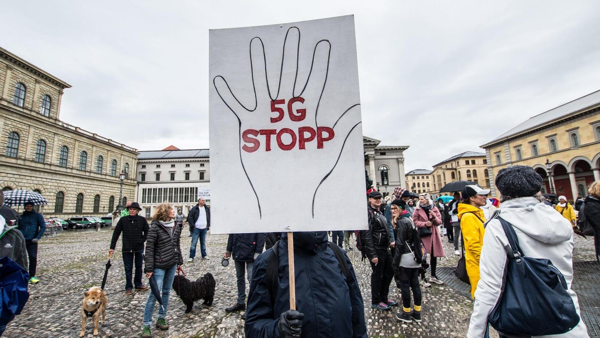 Ein Mensch verdeckt sein Gesicht mit einem großen Demoschild, auf dem eine Hand aufgemalt ist und '5G STOPP' steht. Ein Mensch verdeckt sein Gesicht mit einem großen Demoschild, auf dem eine Hand aufgemalt ist und '5G STOPP' steht.