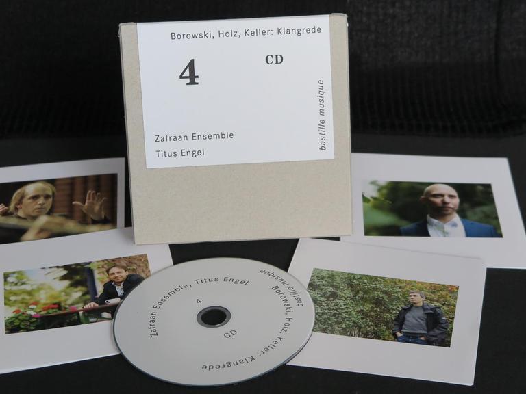 Eine CD liegt ausgepackt mit Cover und Booklets auf schwarzem Hintergrund