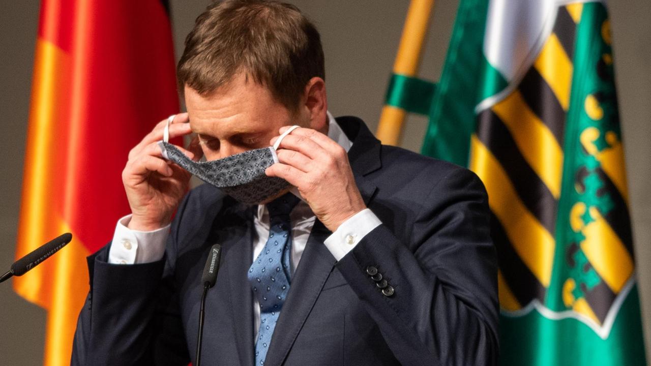Sachsens Ministerpräsident Michael Kretschmer (CDU) zieht nach seiner Rede in einer Sondersitzung des Sächsischen Landtages seinen Mundschutz an. Sachsens Ministerpräsident Michael Kretschmer (CDU) zieht nach seiner Rede in einer Sondersitzung des Sächsischen Landtages seinen Mundschutz an.