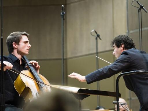 Der Cellist spielt auf seinem Instrument, neben ihm ist der Dirigent in Aktion zu sehen.
