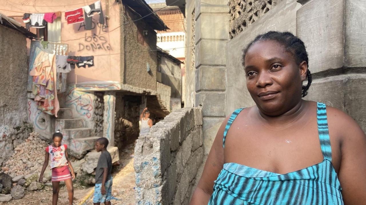 Ein Frau mit einem gestreiften Sommerkleid lehnt an eine Mauer. Im Hintergrund hängt Wäsche zwischen zwei Häusern, zwei Kinder spielen. Ein Frau mit einem gestreiften Sommerkleid lehnt an eine Mauer. Im Hintergrund hängt Wäsche zwischen zwei Häusern, zwei Kinder spielen.