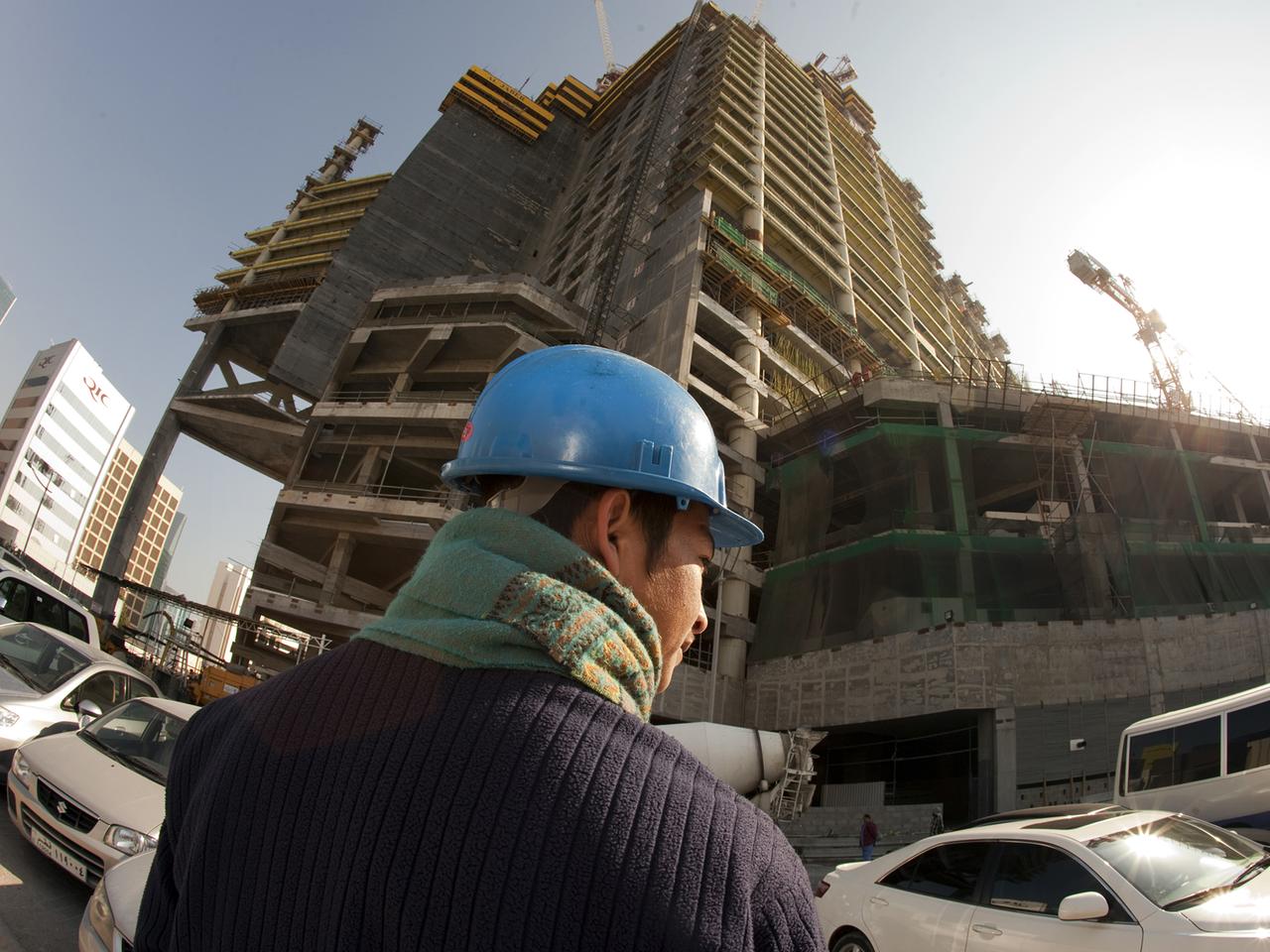 Ein asiatischer Arbeiter mit blauem Schutzhelm steht auf einer Baustelle in Doha