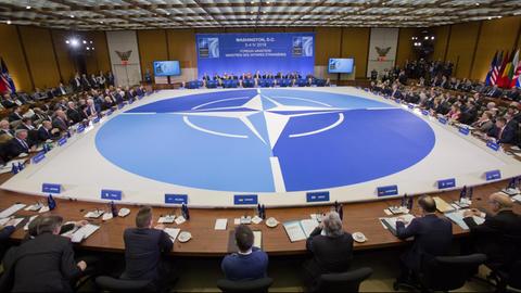Blick auf den großen viereckigen Tisch mit der Nato-Windrose, an dem die Teilnehmer sitzen.
