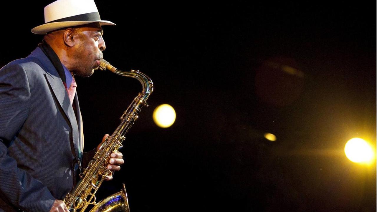 Der Saxofonist Archie Shepp steht auf einer Bühne und spielt sein Instrument, auf der rechten Seite ist ein Scheinwerfer zu sehen, der den Musiker anstrahlt. Der Saxofonist Archie Shepp steht auf einer Bühne und spielt sein Instrument, auf der rechten Seite ist ein Scheinwerfer zu sehen, der den Musiker anstrahlt.