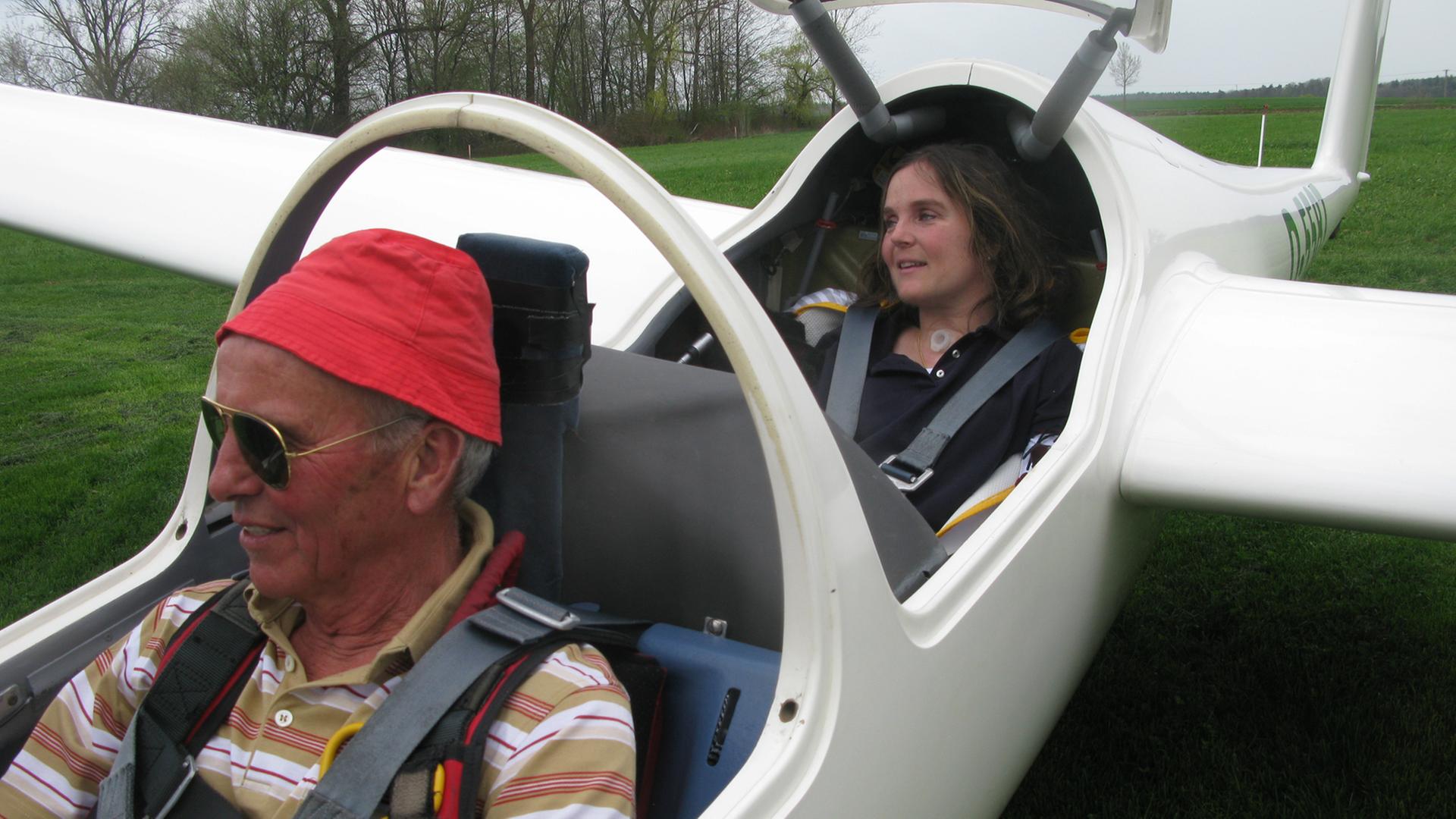 Detlef Glätzer und Maria-Cristina Hallwachs. Ein Mann und eine Frau sitzen hintereinander in einem parkendem Sportflugzeug.