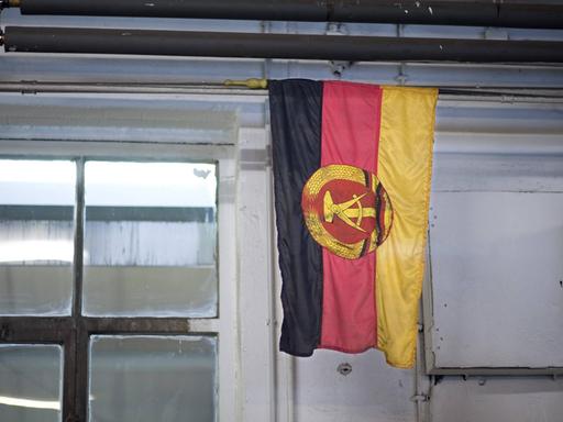 Eine Flagge der ehemaligen DDR hängt in einem Raum mit Fenster.
