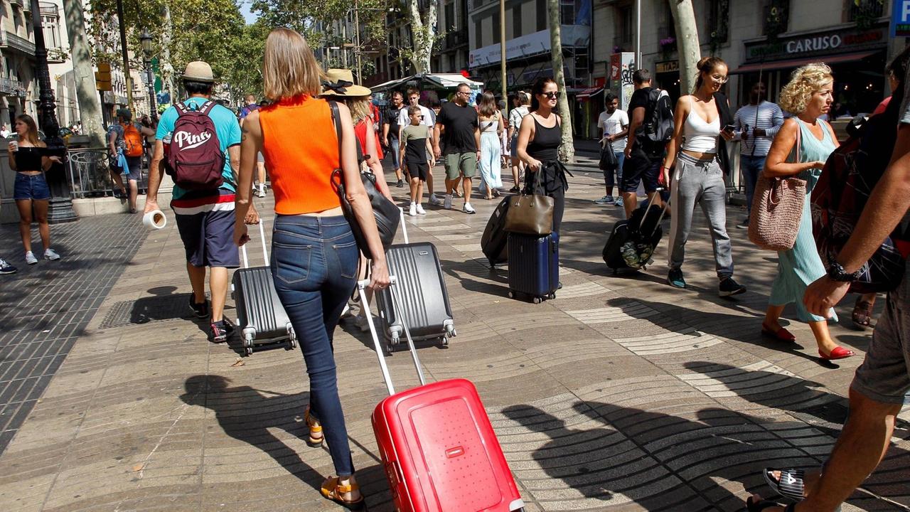 Mehrere Touristen schlängeln sich im Sommer 2019 mit Rollkoffern durch eine Einkaufsstraße in Barcelona.