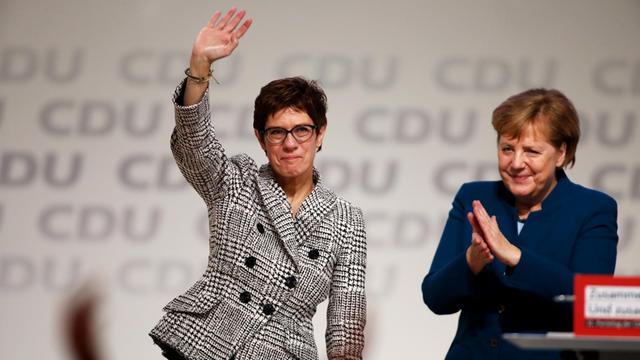 Annegret Kramp-Karrenbauer winkt auf dem Parteitag den Delegierten zu, neben ihr applaudiert Angela Merkel