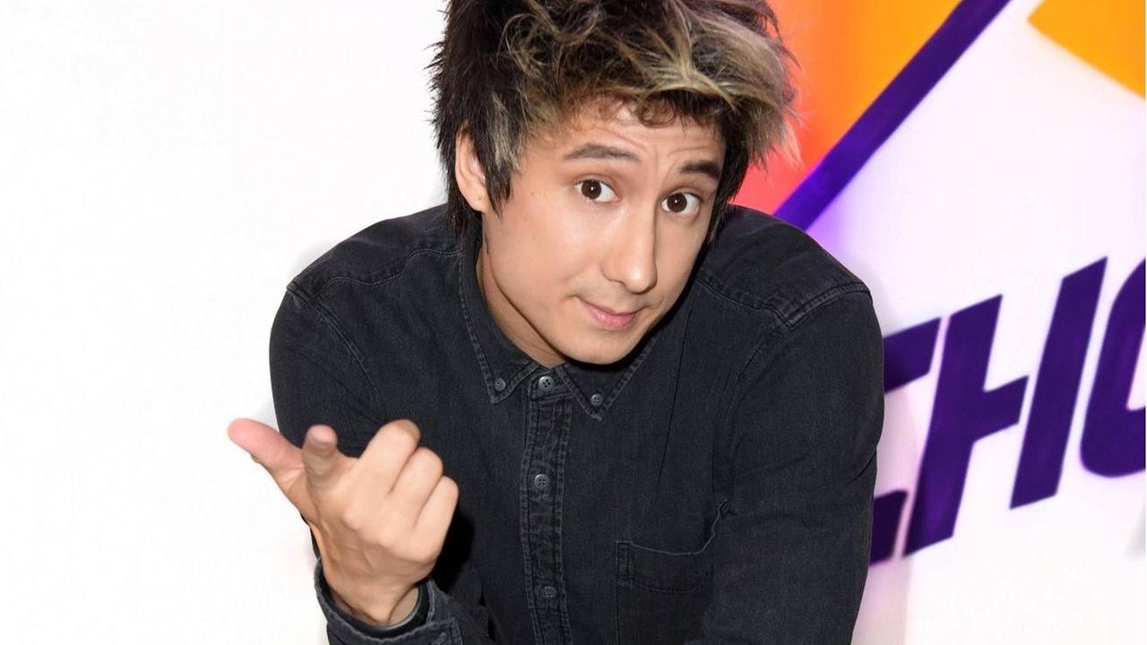 Julien Bam, gekleidet in schwarze Kleidung und mit roten Badelatschen, kniet vor einem Aufsteller. Julien Bam, gekleidet in schwarze Kleidung und mit roten Badelatschen, kniet vor einem Aufsteller.