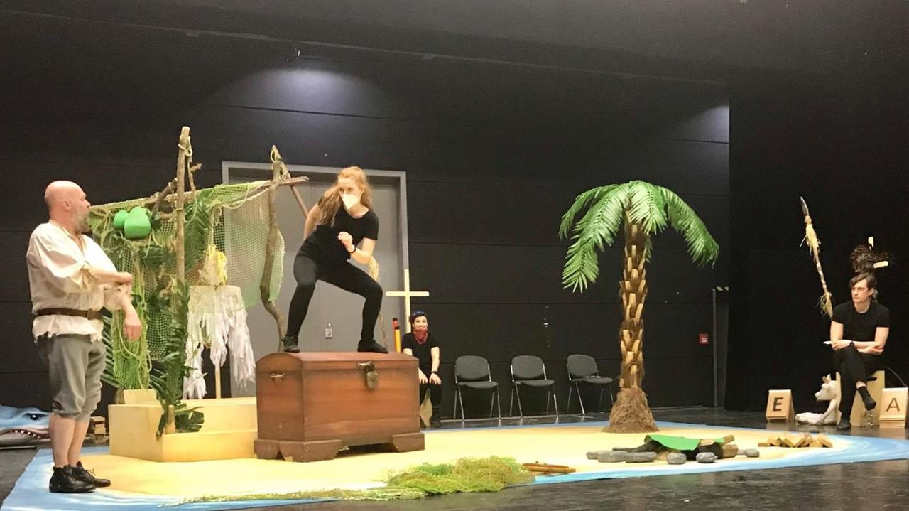 Eine in schwarz gekleidete Frau, Schauspielerin Katarzyna Kunicka, steht auf der Bühne auf einer Holzkiste. Links schaut ein Mann in ihre Richtung. Eine in schwarz gekleidete Frau, Schauspielerin Katarzyna Kunicka, steht auf der Bühne auf einer Holzkiste. Links schaut ein Mann in ihre Richtung.