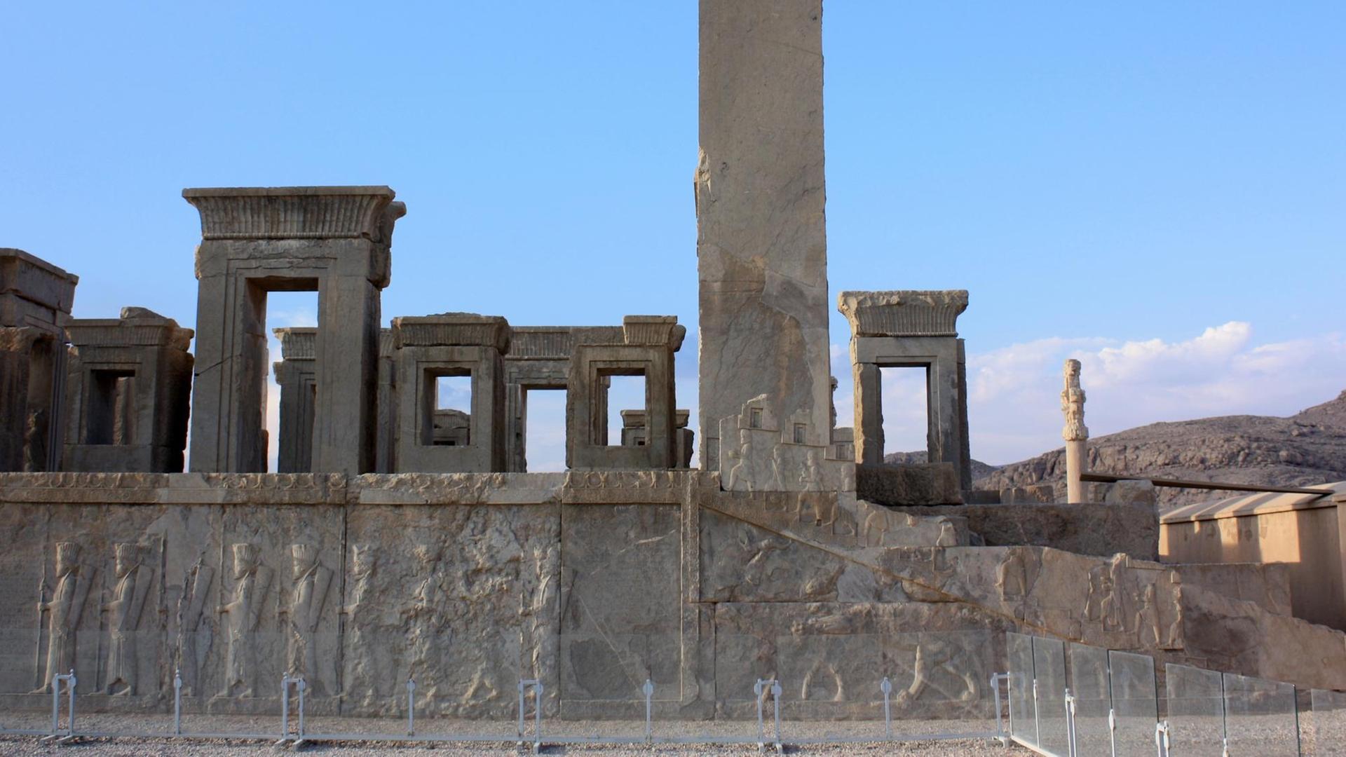 Ruinen mit gut erhaltenen Reliefs iin der altpersischen Stadt Persepolis vor blauem Himmel.