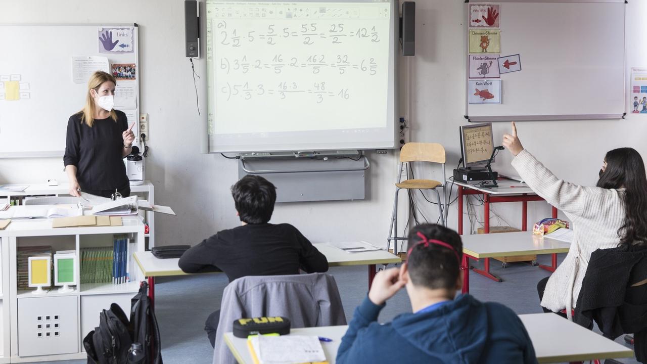 Schüler sitzen vor ihrer Lehrerin im Klassenraum, neben der Lehrerin steht ein Whiteboard, daneben ein Computer. Schüler sitzen vor ihrer Lehrerin im Klassenraum, neben der Lehrerin steht ein Whiteboard, daneben ein Computer.