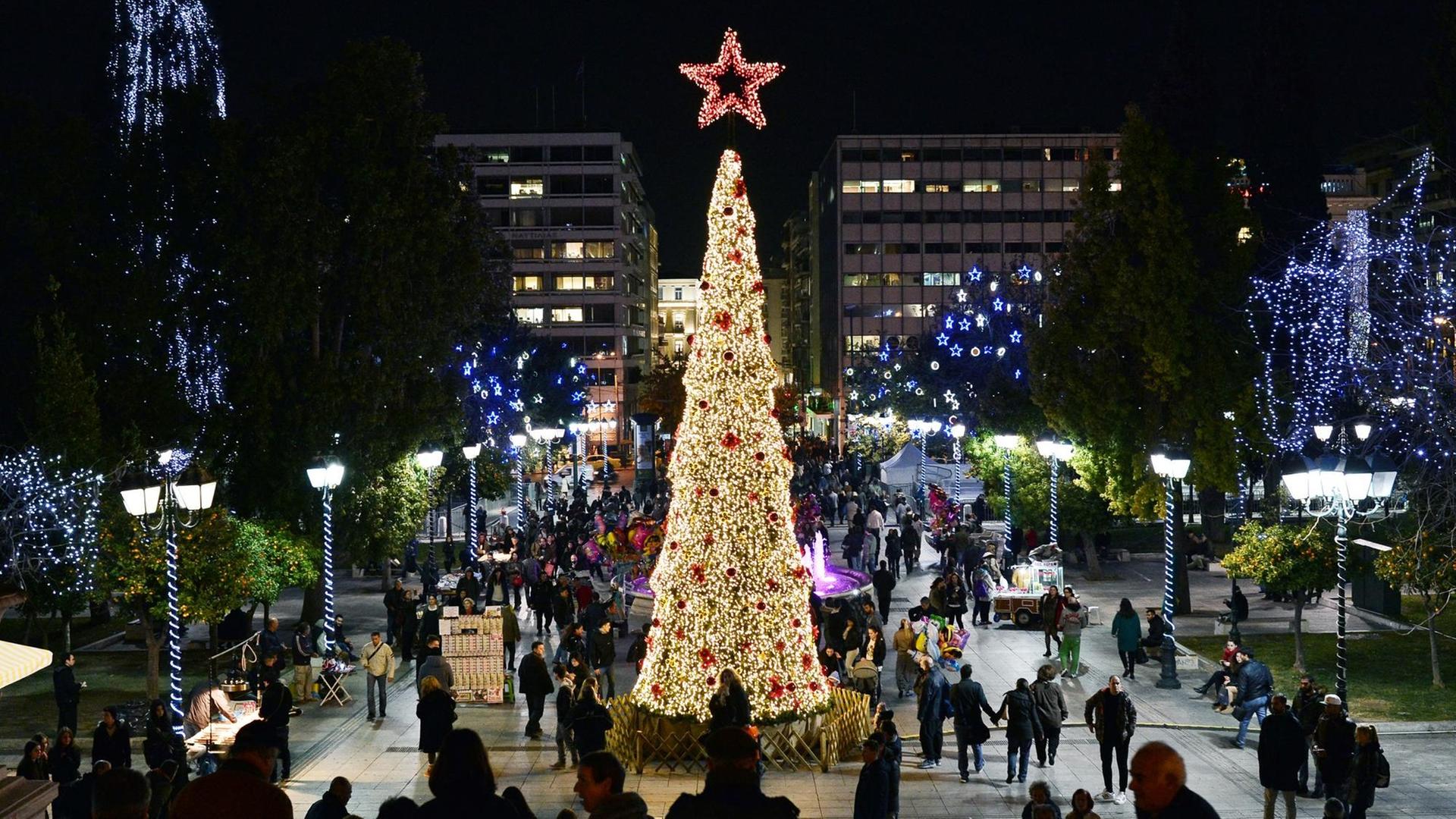 Menschen laufen über den weihnachtlich geschmückten Syntagma-Platz in Athen, der vor dem griechischen Parlament liegt und einen Weihnachtsbaum in der Mitte hat.