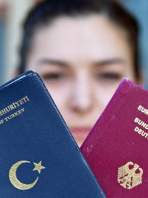 Eine junge Frau hält einen türkischen und einen deutschen Reisepass in den Händen.