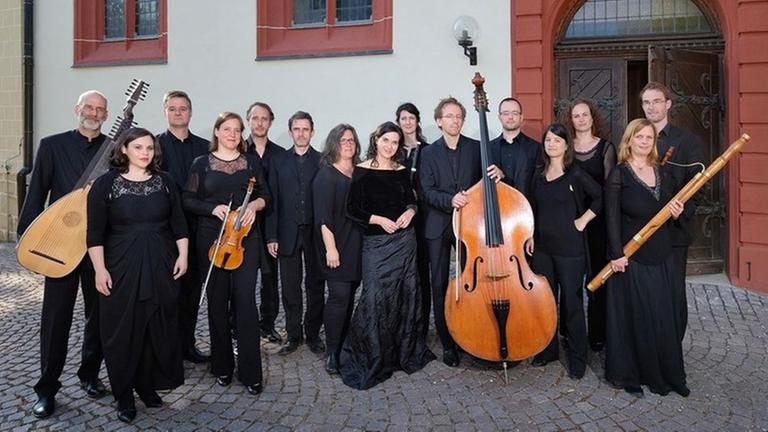 Musiker mit alten Instrumenten und Sängerinnen stehen vereint vor einem historischen Gebäude. Musiker mit alten Instrumenten und Sängerinnen stehen vereint vor einem historischen Gebäude.