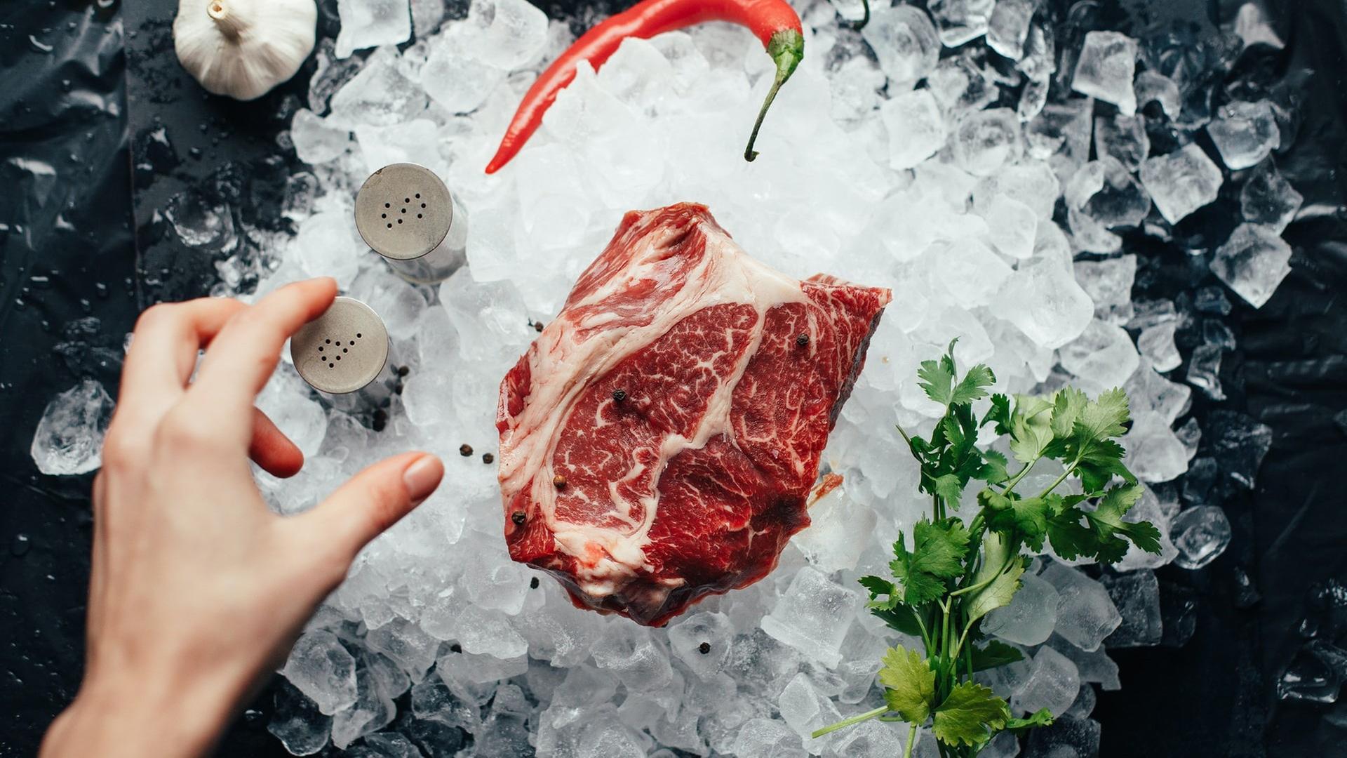 Eine Hand greift nach einem rohen Stück Fleisch. Eine Hand greift nach einem rohen Stück Fleisch.