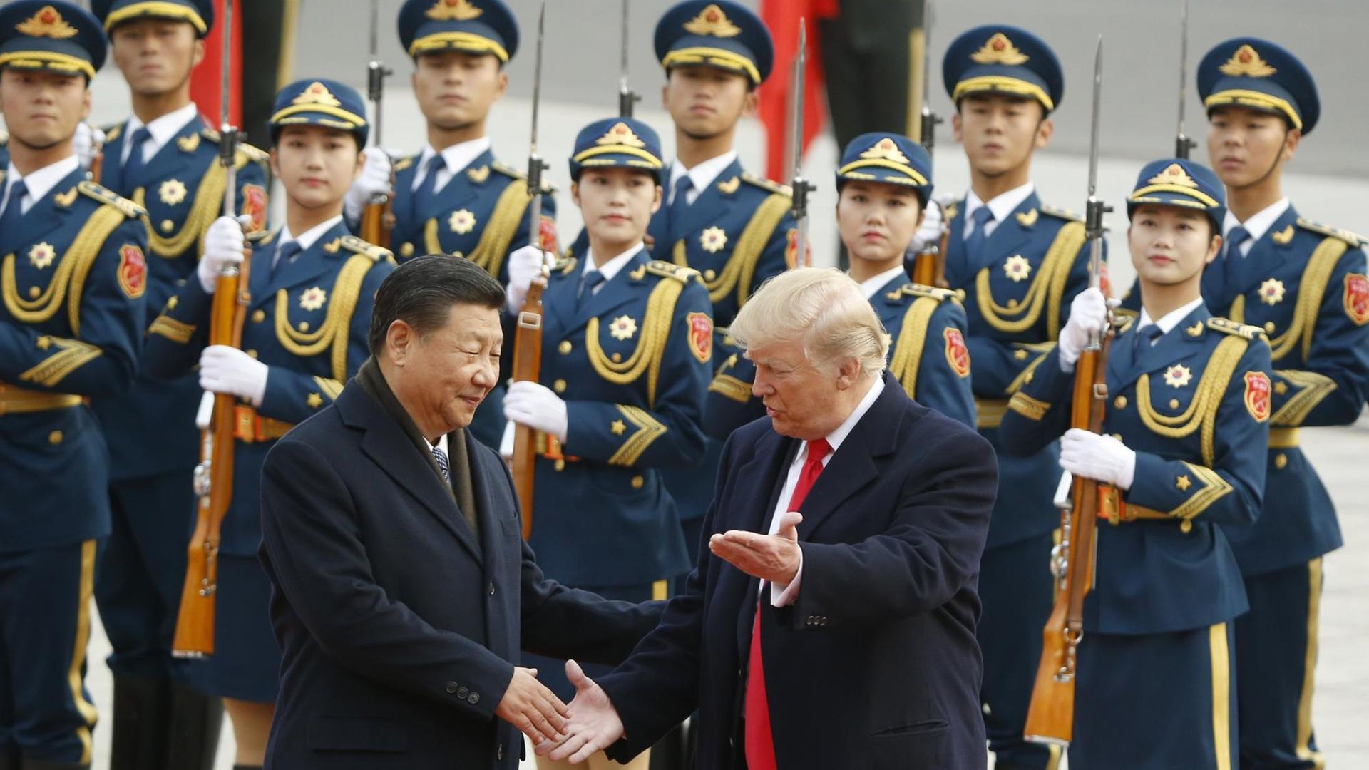 Xi Jinping begrüßt Donald Trump während einer Zeremonie in Peking 2017, im Hintergrund stehen Soldaten Spalier.