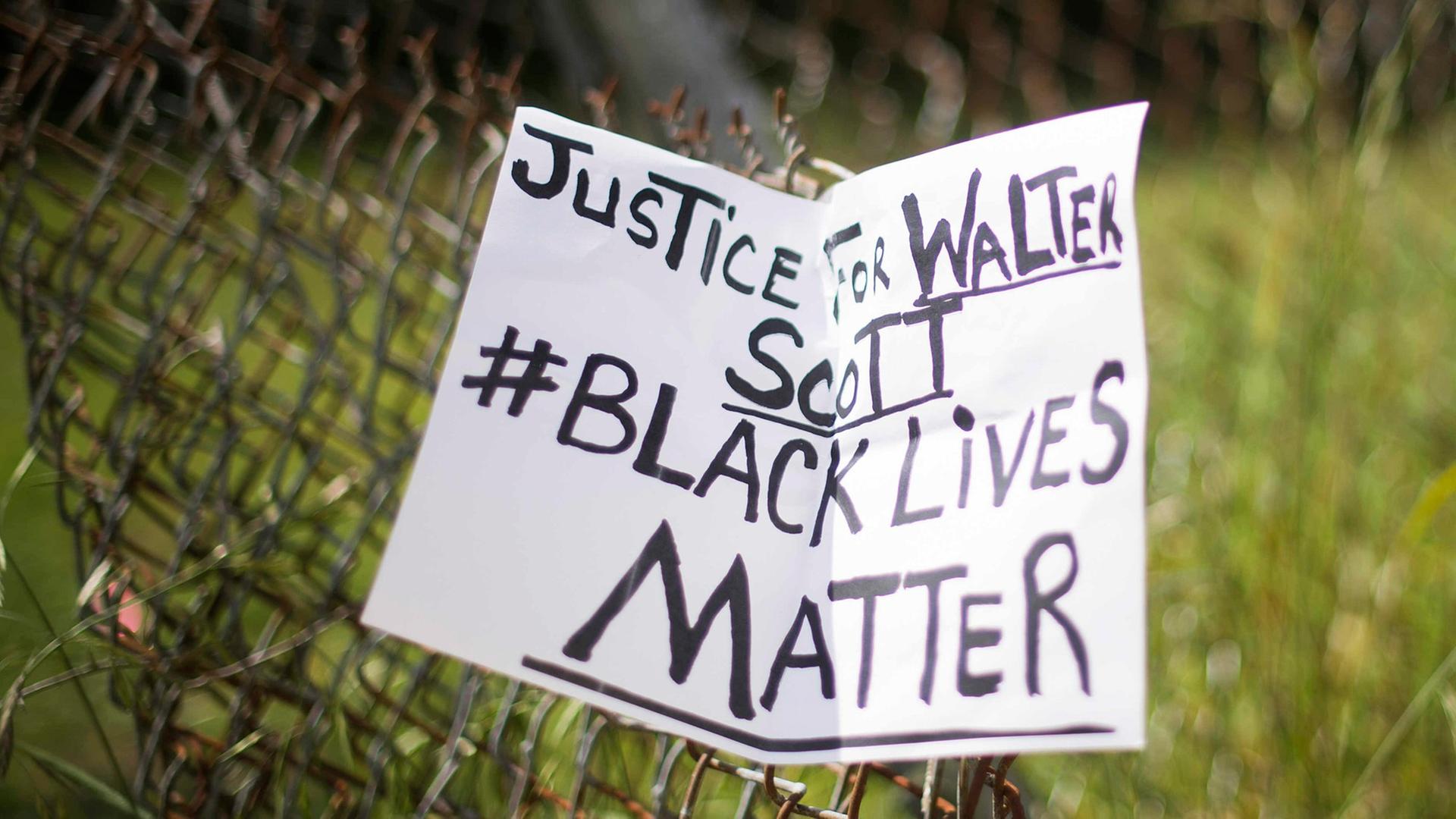 Ein handgeschriebener Zettel hängt an einem Maschendrahtzaun. Aufschrift: "Justice for Walter Scott - black lives matter"