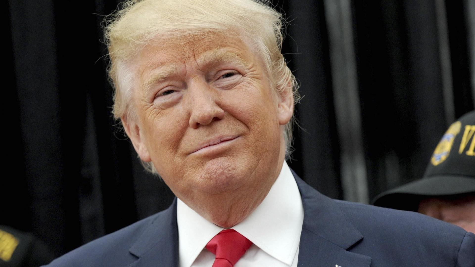 Porträt von Donald Trump. Er trägt einen dunklen Anzug und eine rote Krawatte