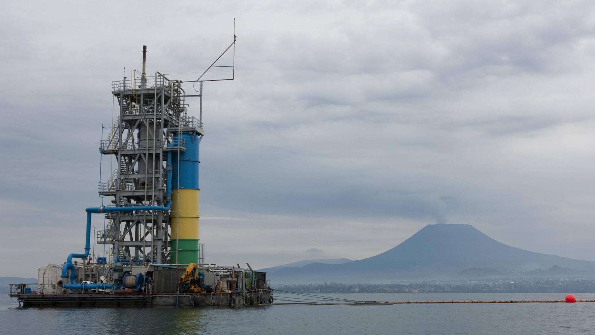 Auf einem See wird eine große Gasförderstation gebaut, im Hintergrund thront ein großer Vulkan über dem See. Auf einem See wird eine große Gasförderstation gebaut, im Hintergrund thront ein großer Vulkan über dem See.
