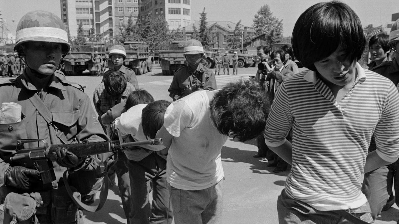 Schwarzweißaufnahme von bewaffneten Soldaten, die protestierende Studenten abführen.