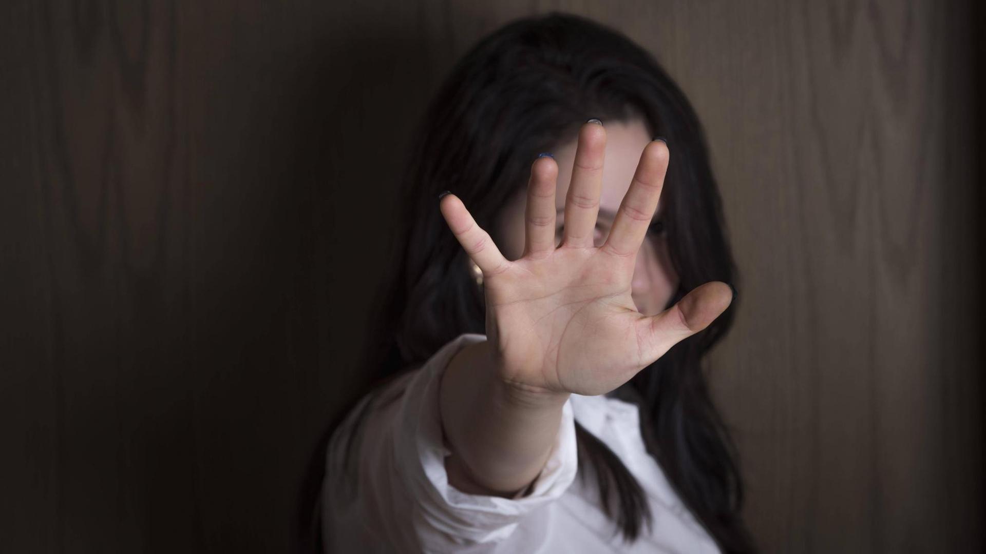 Eine Frau vor einer Holzwand hat ihre Hand zu einer Stopp-Geste ausgestreckt, und verdeckt so ihr Gesicht. Eine Frau vor einer Holzwand hat ihre Hand zu einer Stopp-Geste ausgestreckt, und verdeckt so ihr Gesicht.