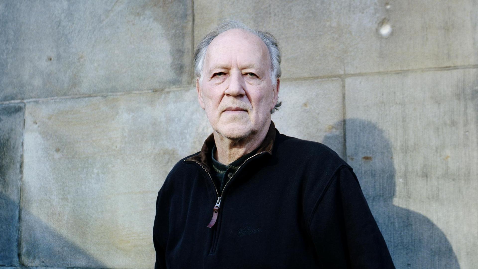 Porträt von Werner Herzog vor einer Mauer aus Stein.
