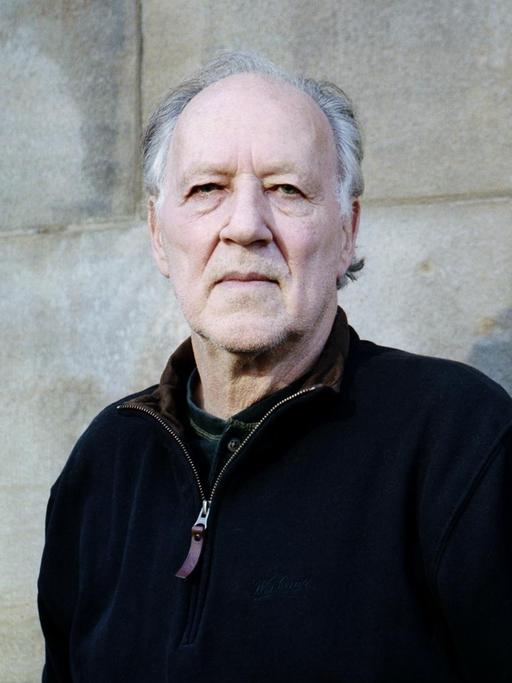 Porträt von Werner Herzog vor einer Mauer aus Stein.