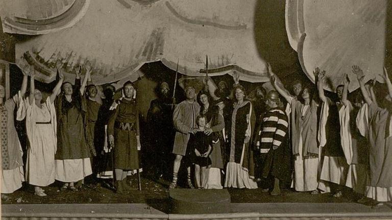 Schwarzweißaufnahme von 1920: Darsteller der Händel-Oper "Rodelinde" stehen in Kostümen zum Schlussbild auf der Bühne versammelt. Schwarzweißaufnahme von 1920: Darsteller der Händel-Oper "Rodelinde" stehen in Kostümen zum Schlussbild auf der Bühne versammelt.