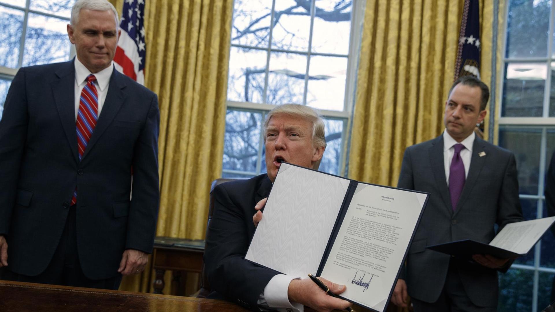 US-Präsident Donald Trump (m.) mit dem Dektret zum Ausstieg aus dem Handelsabkommen TPP. Links ist Vize-Präsident Mike Pence, rechts ist der Stabschef im Weißen Haus, Reince Priebus, zu sehen.
