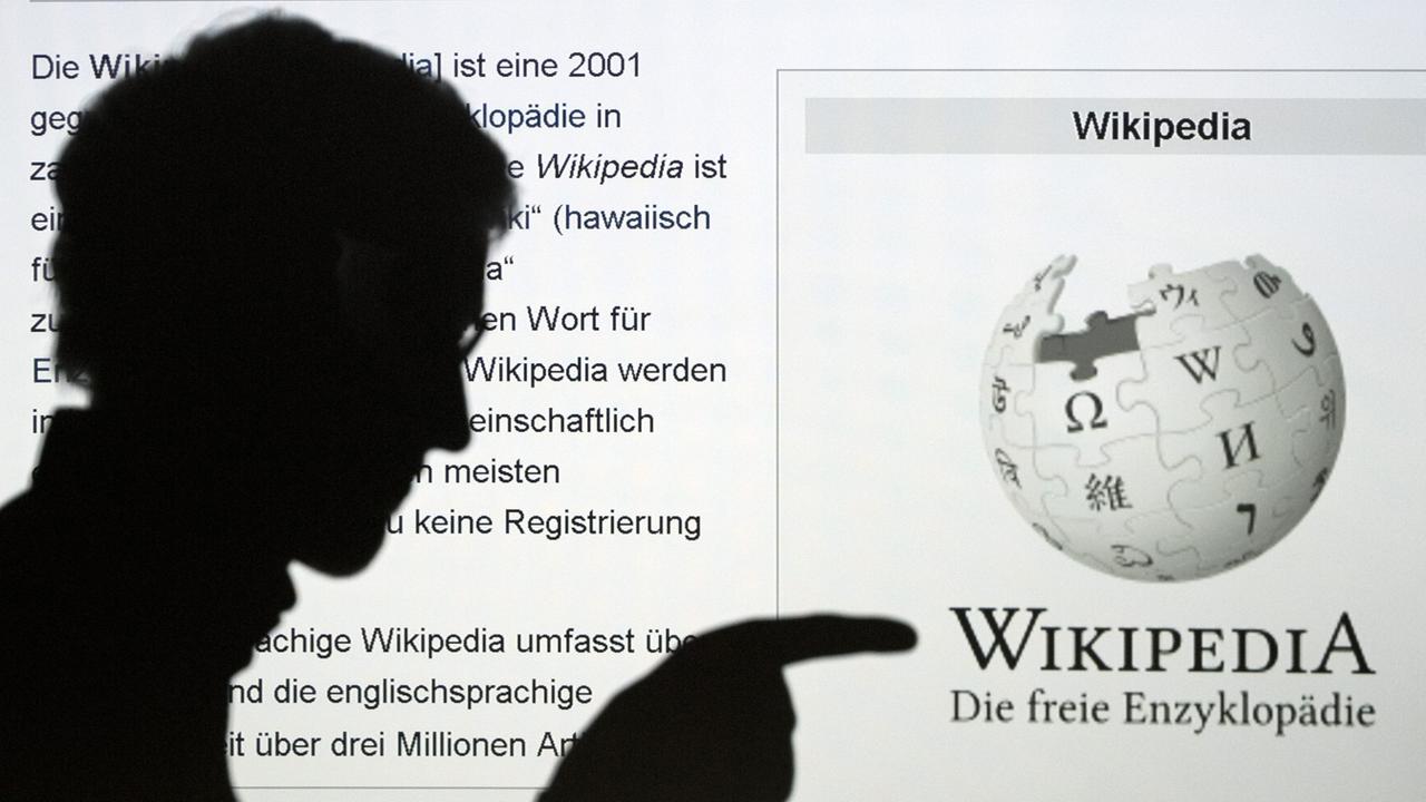Die Silhouette eines Mannes, der mit seinem Finger auf das Wort Wikipedia zeigt, ist vor der Internetseite der Online-Enzyklopädie Wikipedia zu sehen.