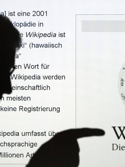 Die Silhouette eines Mannes, der mit seinem Finger auf das Wort Wikipedia zeigt, ist vor der Internetseite der Online-Enzyklopädie Wikipedia zu sehen.