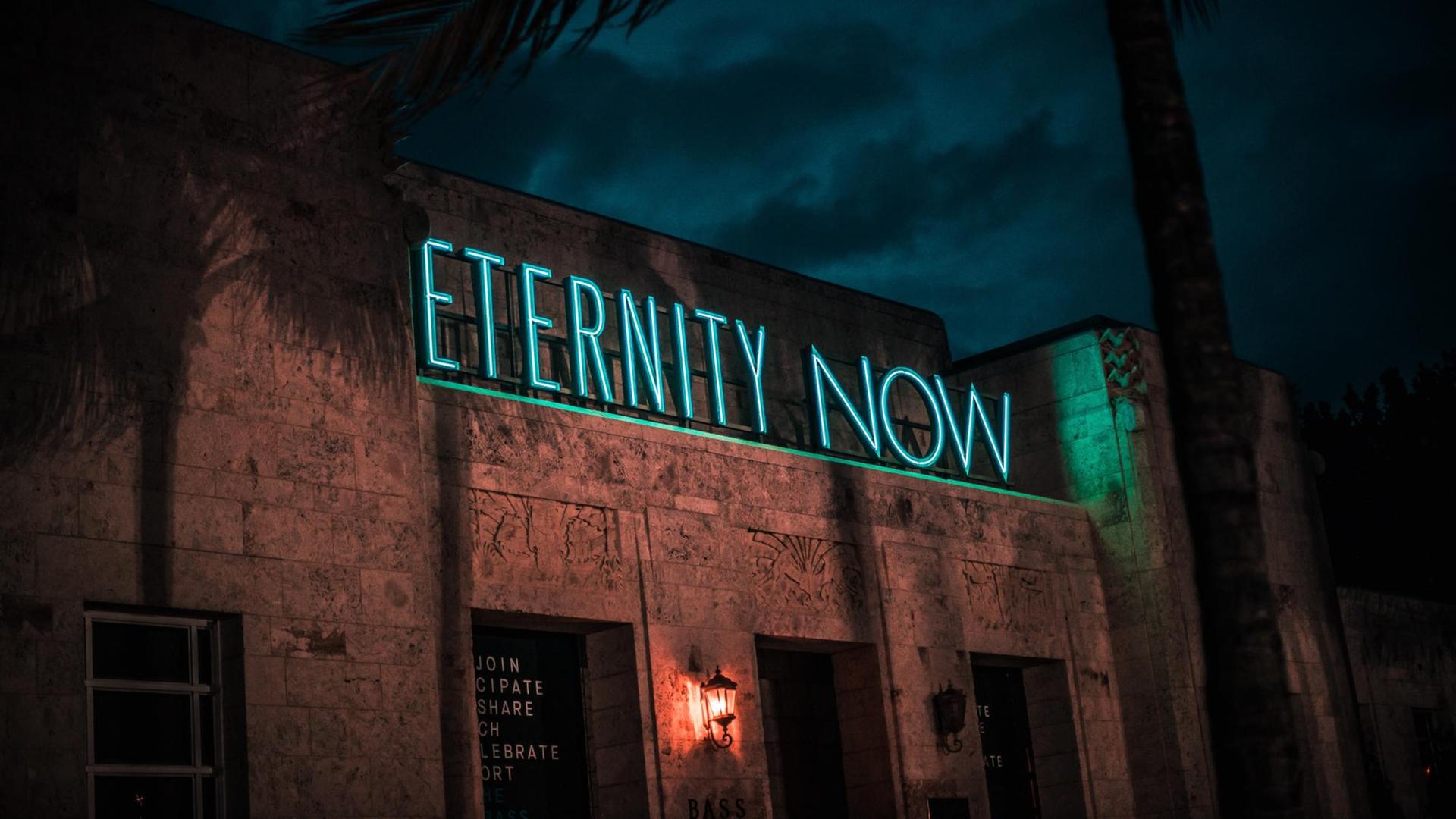 Gebäude bei Nacht mit Leuchtschrift "Eternity now"