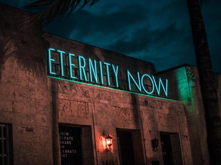 Gebäude bei Nacht mit Leuchtschrift "Eternity now"