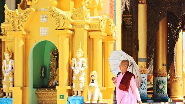 Eine Nonne mit Regenschirm (Sonnenschirm) geht durch die Shwedagon Pagode in der Stadt Yangon in Myanmar.