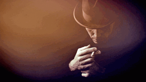Porträt eines jungen Mannes mit Hut und Zigarette in der Hand, der Blick nach unten gerichtet.