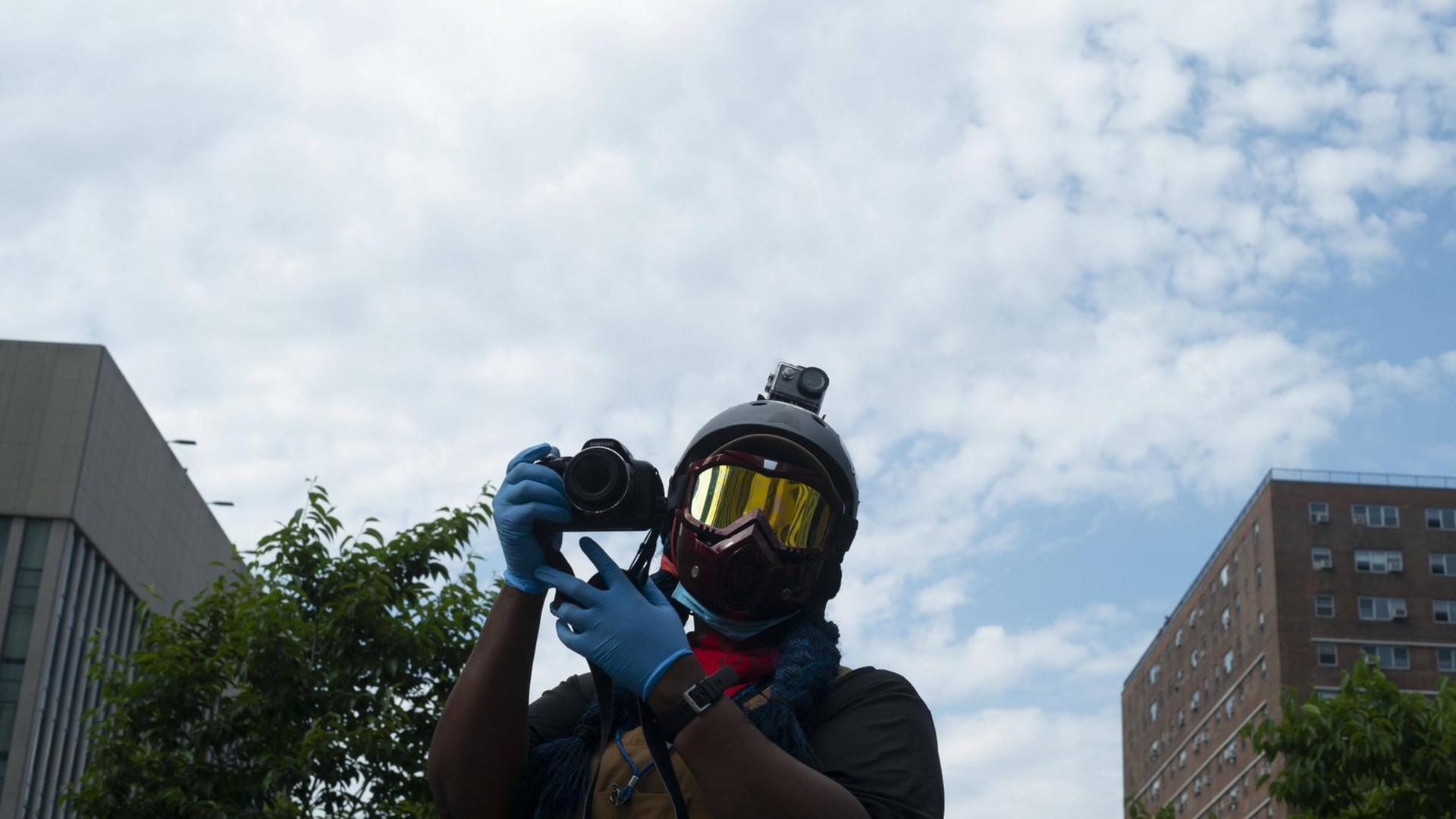Eine Person mit Helm, Schutzbrille und Kamera dokumentiert in New York eine Demonstration gegen Polizeigewalt Eine Person mit Helm, Schutzbrille und Kamera dokumentiert in New York eine Demonstration gegen Polizeigewalt